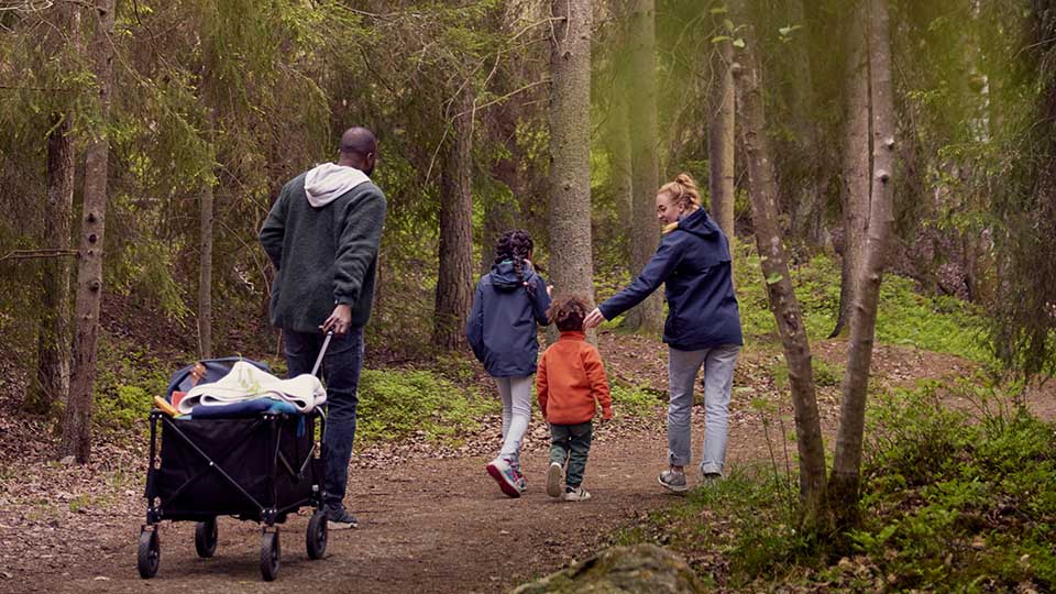 Familj med tv&aring; barn promenerar i skogen och drar en campingvagn efter sig. Sverige