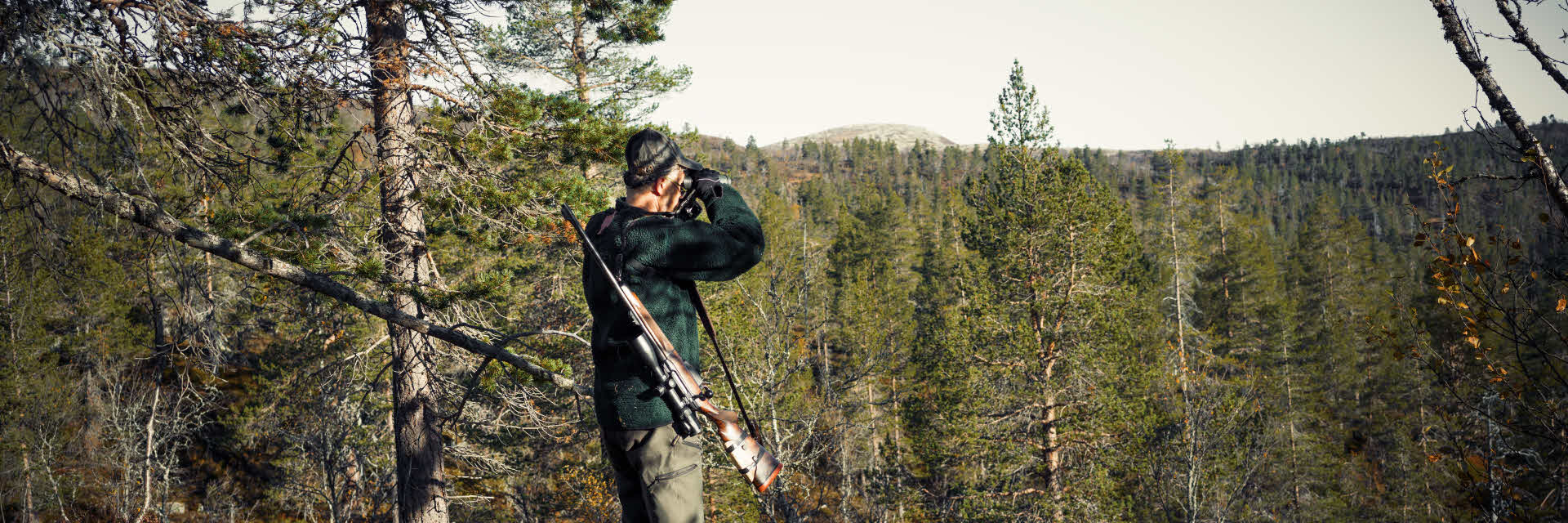 Jägare med kikare som spejar ut över en skogsbrant.