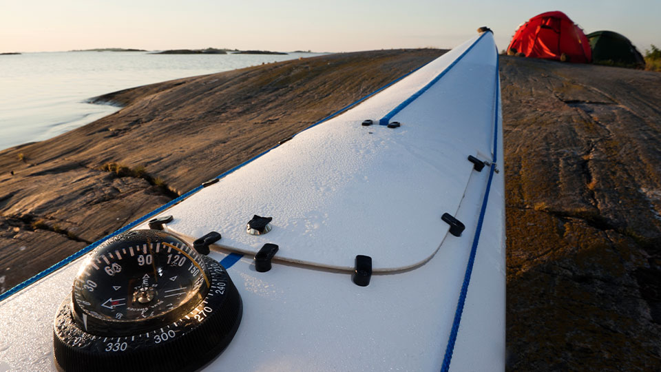 Kompass och fören på en kajak på en klipphäll med tält.