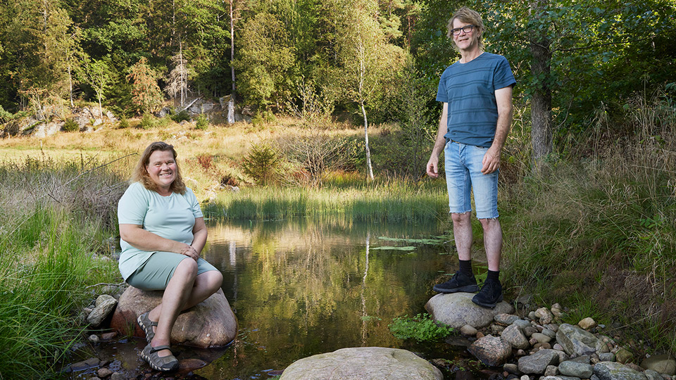 Två personer fotade vid vatten på  en äng