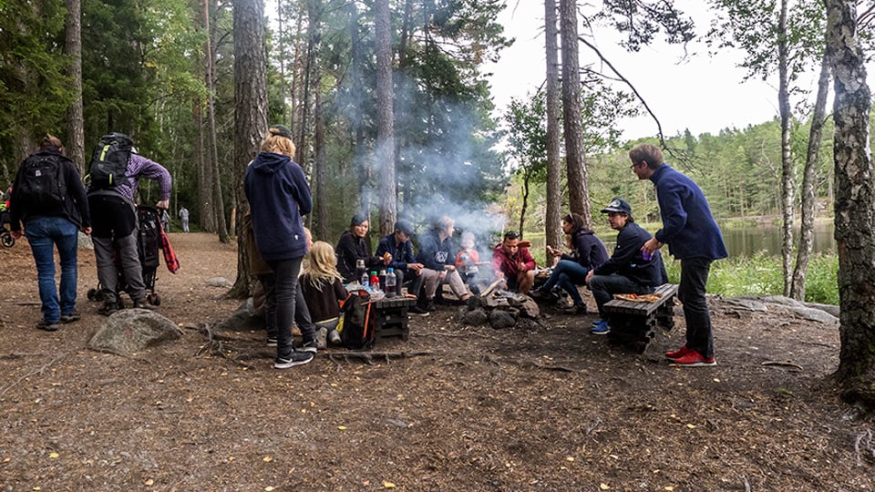 Ett sällskap har picknik runt en öppen eld, rastplats i Tyresta nationalpark
