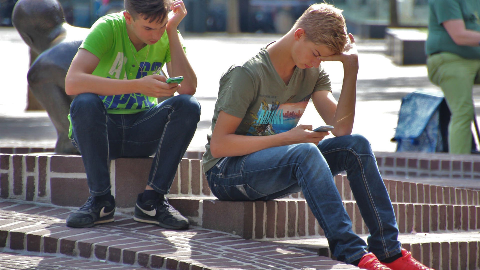 Två ungdomar sitter med mobilen i en park. 